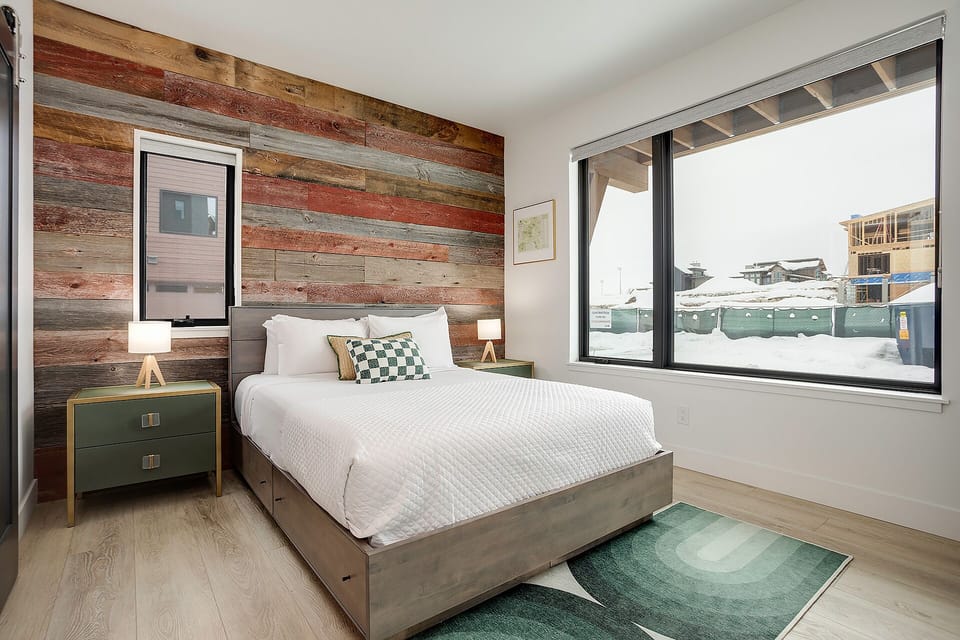 Wake up to snowy mountain views from your modern bedroom with rustic wood accent wall and cozy furnishings.
