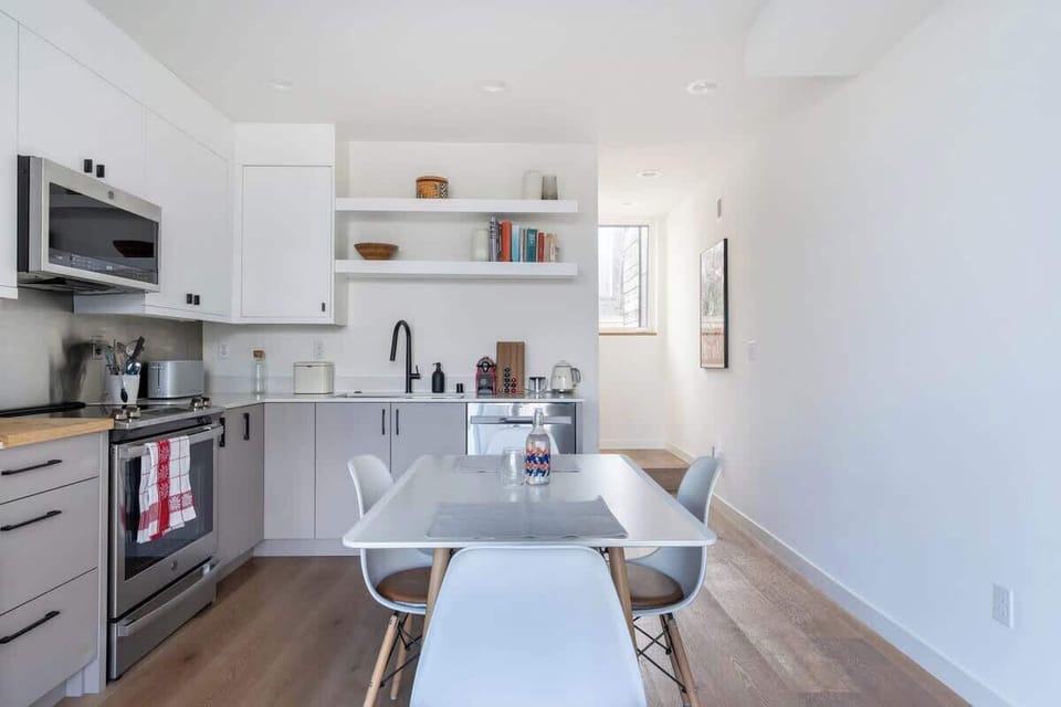 Bright, modern kitchen with sleek cabinetry, open shelving, stainless appliances, and a cozy dining table in an airy layout.