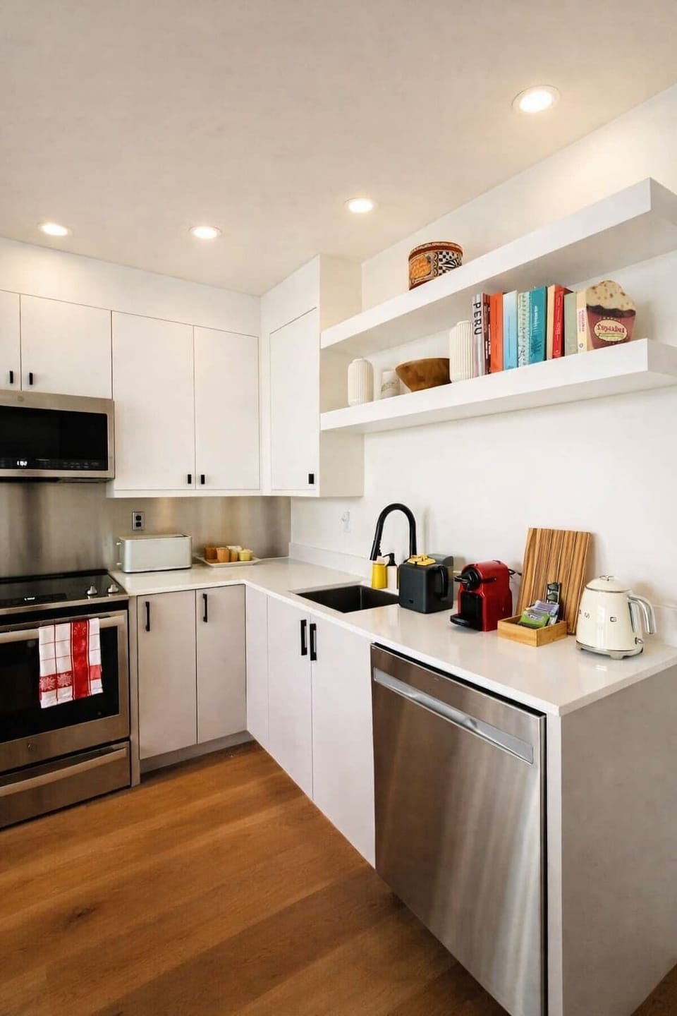 Bright modern kitchen with sleek white cabinetry, stainless appliances, open shelving, and warm wood floors for a clean, inviting feel.