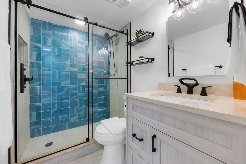 Modern bathroom featuring a glass shower with blue tile accents and black fixtures.