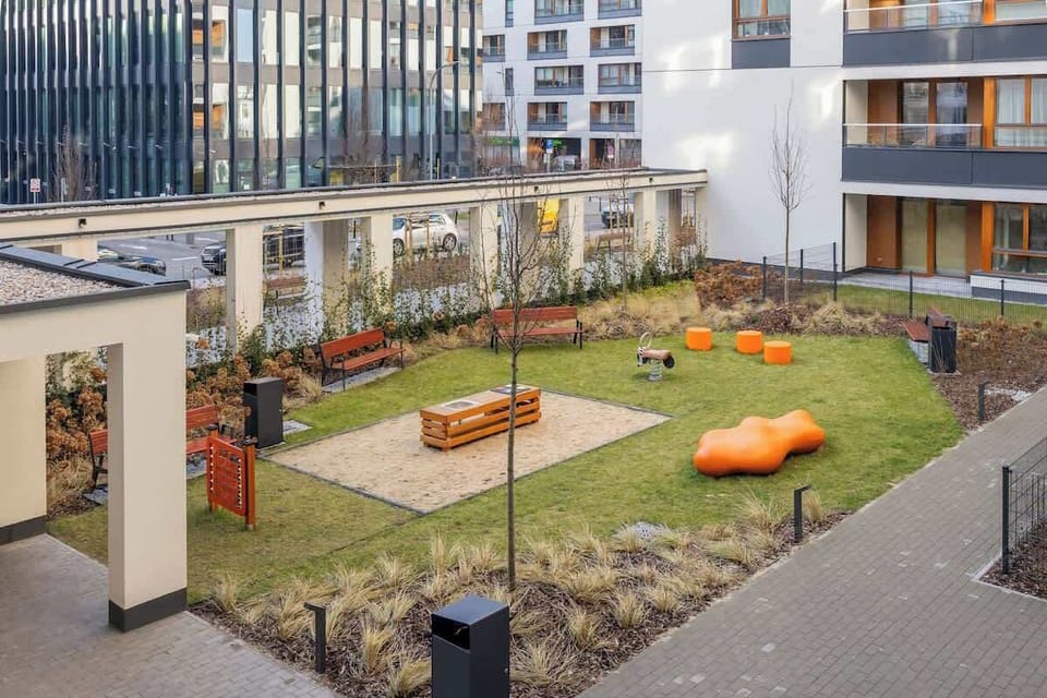 A vibrant courtyard with a well-maintained garden, featuring green spaces, playground equipment, and modern apartment balconies overlooking the area.

