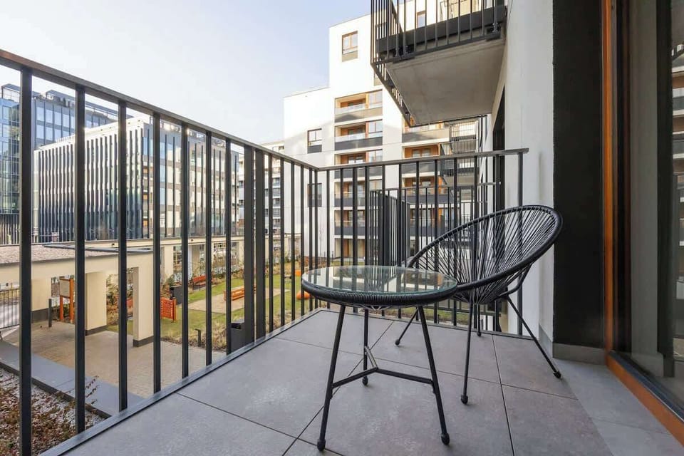 A balcony seating area with a black metal chair and matching table, overlooking the modern apartment complex, providing a relaxing outdoor space.

