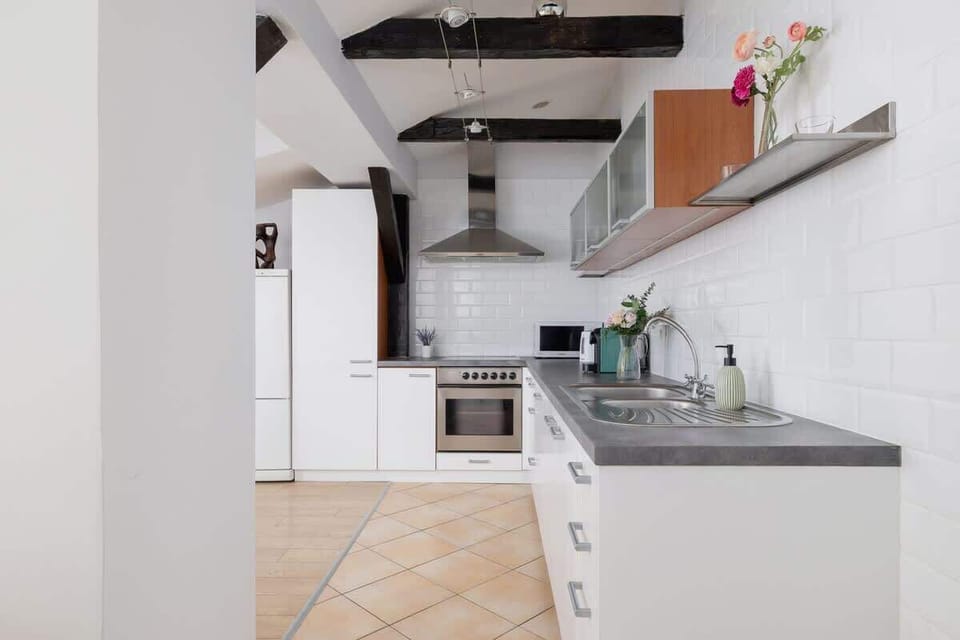 A different perspective of the kitchen, with white-tiled backsplash, a modern extractor hood, and a compact stove.


