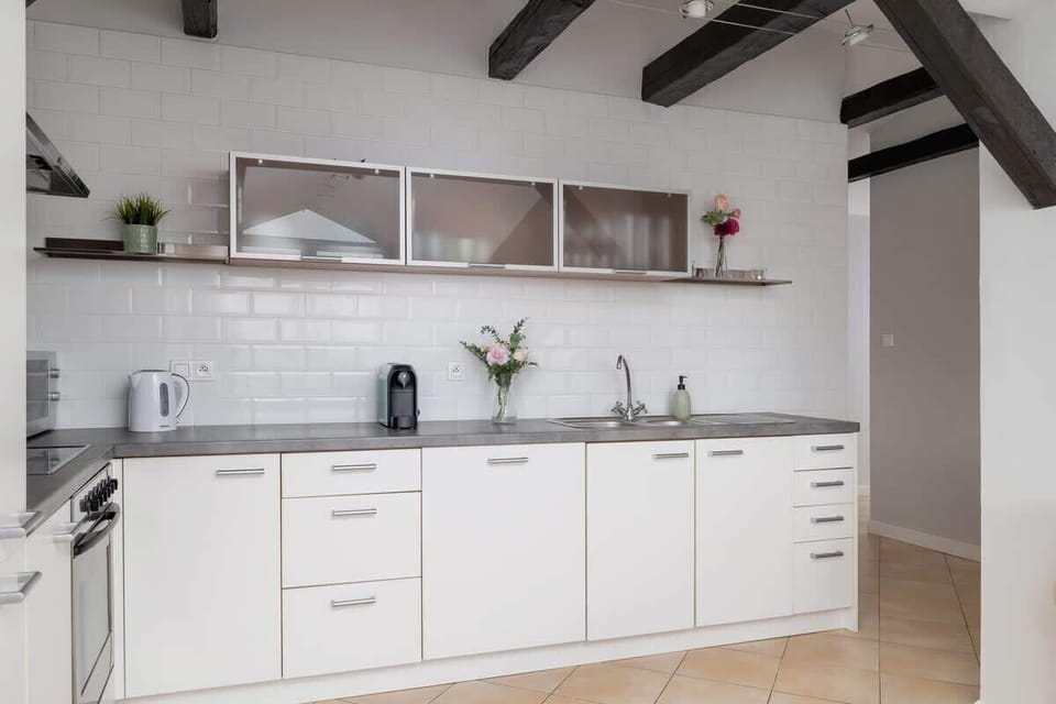 A modern kitchen with white cabinets, open shelving, and wooden ceiling beams, offering ample storage and counter space.

