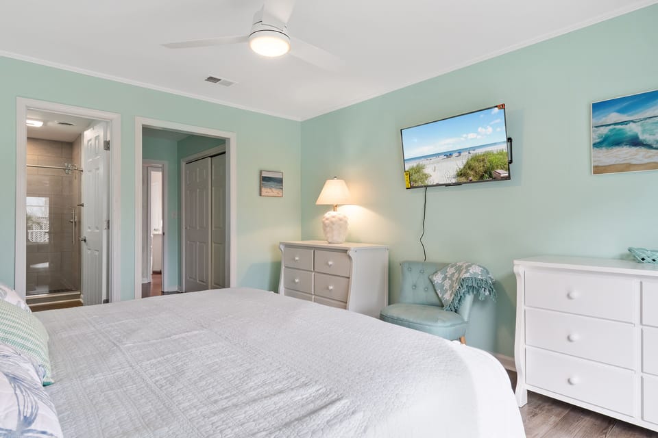 Drift off in this serene bedroom featuring soothing sea-glass walls, crisp white linens, and coastal-themed TV for your evening relaxation.