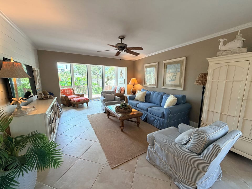 Unwind in your coastal-inspired living space with soft seating, natural light, and breezy ceiling fan—perfect for lazy afternoons after exploring the area.