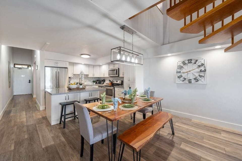 Open‑concept living room featuring a cozy seating arrangement, vaulted ceilings, and an elegant wood staircase connecting to the loft.