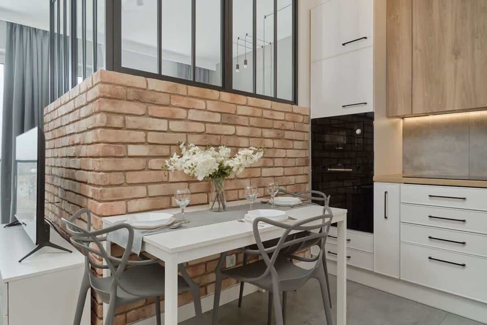 A dining area with a rustic brick wall, a glass dining table with metal chairs, and stylish decor elements for an industrial-chic ambiance.

