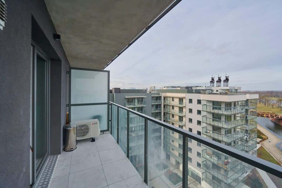 Another angle of the balcony, showing neighboring buildings and an extended view of the cityscape, emphasizing the apartment’s modern urban setting.

