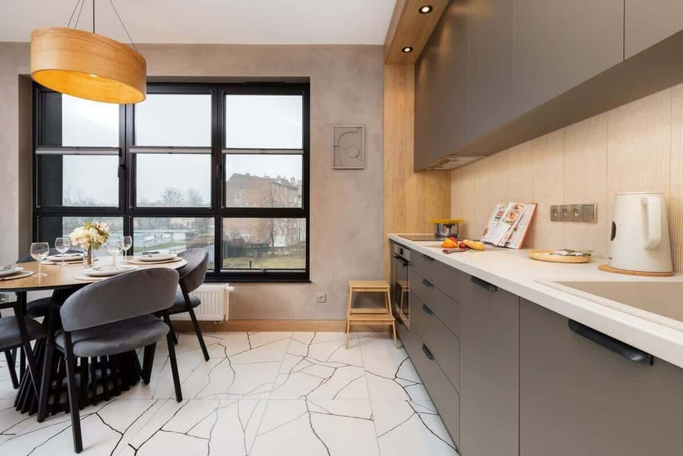 A modern open-plan kitchen with a gray countertop, sleek cabinets, and a large window offering plenty of natural light while cooking.

