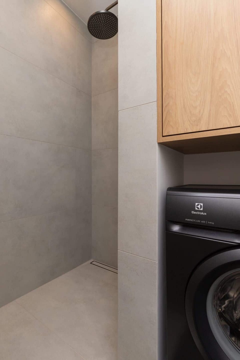 A laundry area with a built-in washing machine, wooden cabinets, and a minimalist gray-tiled wall for a practical yet stylish touch.

