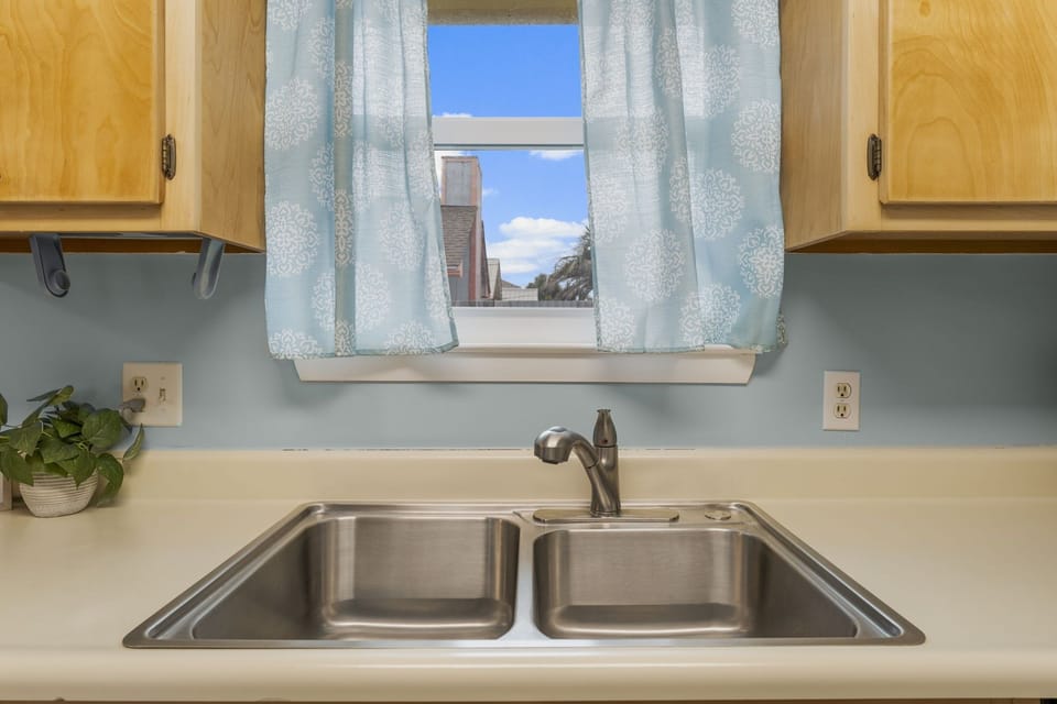 A modern kitchen sink with a view through a window framed by patterned curtains.