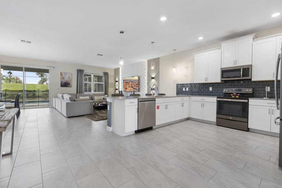 Enjoy cooking in this bright, spacious kitchen with sleek white cabinetry and modern stainless steel appliances. Large windows bring in natural light, creating a warm, inviting atmosphere for all your culinary adventures.
