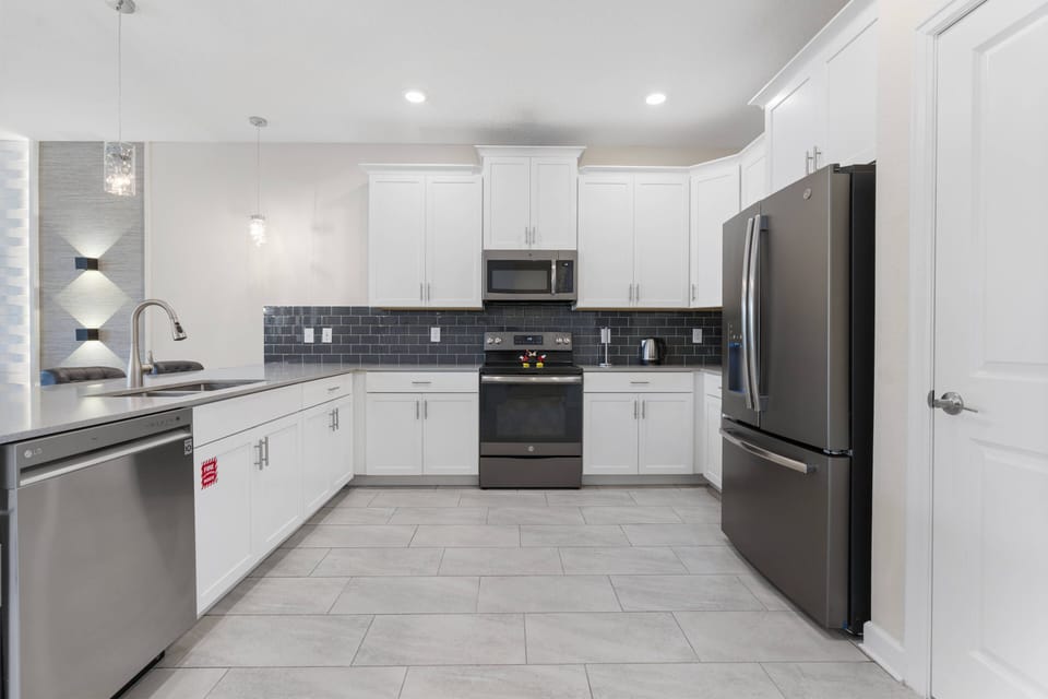 Discover the heart of your stay in this stylish kitchen with stainless steel appliances and sleek white cabinetry, perfectly complemented by modern tile flooring—an ideal space for cooking and casual gatherings.