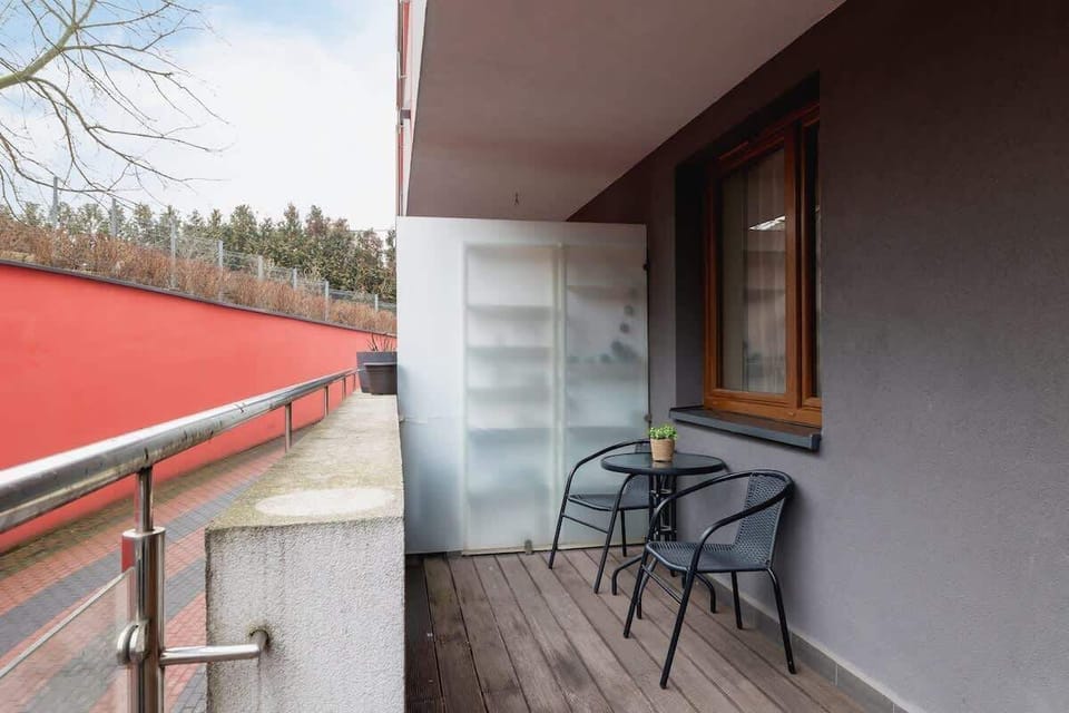 A private balcony with a small table and chairs, featuring a frosted glass divider for privacy and a view of the surrounding area.

