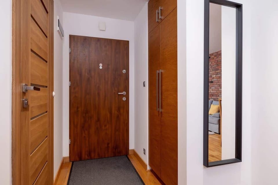 A modern apartment entrance hallway with wooden doors, a full-length mirror, and a sleek minimalist design.

