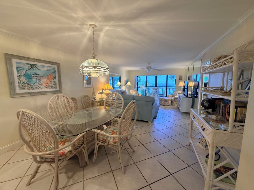 Your coastal getaway features a bright, open-concept space with dining and living areas flowing together, light tile floors, charming beach decor, and windows offering serene ocean views.