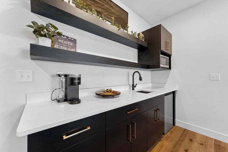 - Brew your morning pick-me-up at the dedicated Keurig coffee nook
- Black cabinetry, gold pulls, and open shelving add stylish function
- Great for storing drinks, prepping snacks, or winding down with wine