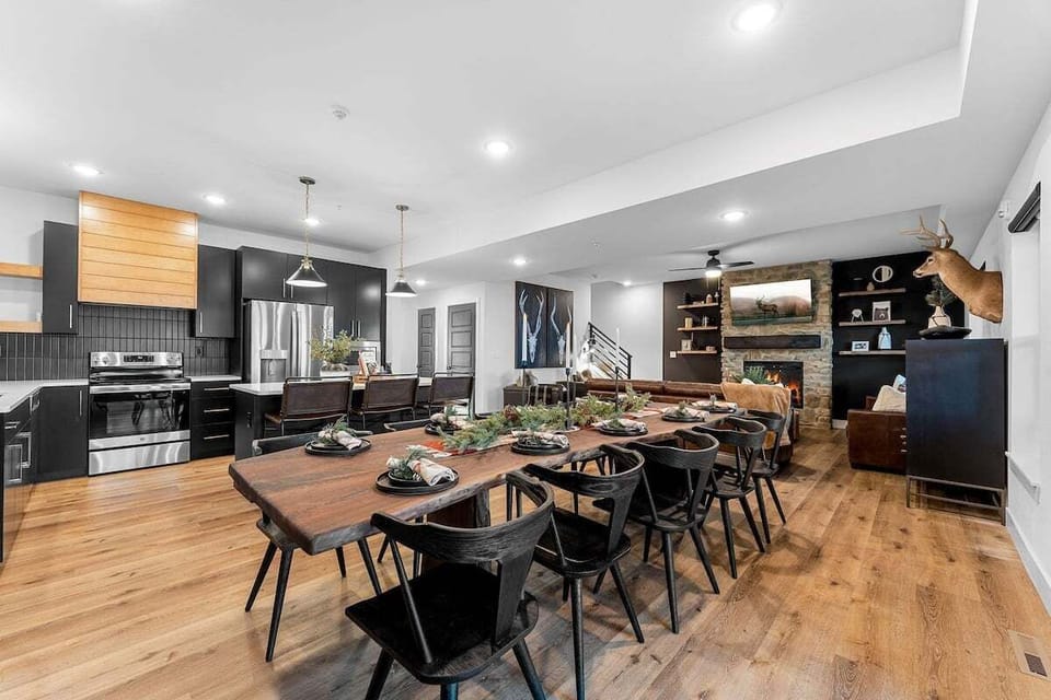 - Host big meals or casual breakfasts around the rustic live-edge table
- Modern black kitchen with wood accents is fully stocked and ready to go
- The open flow leads to a cozy lounge with fireplace and stylish touches
