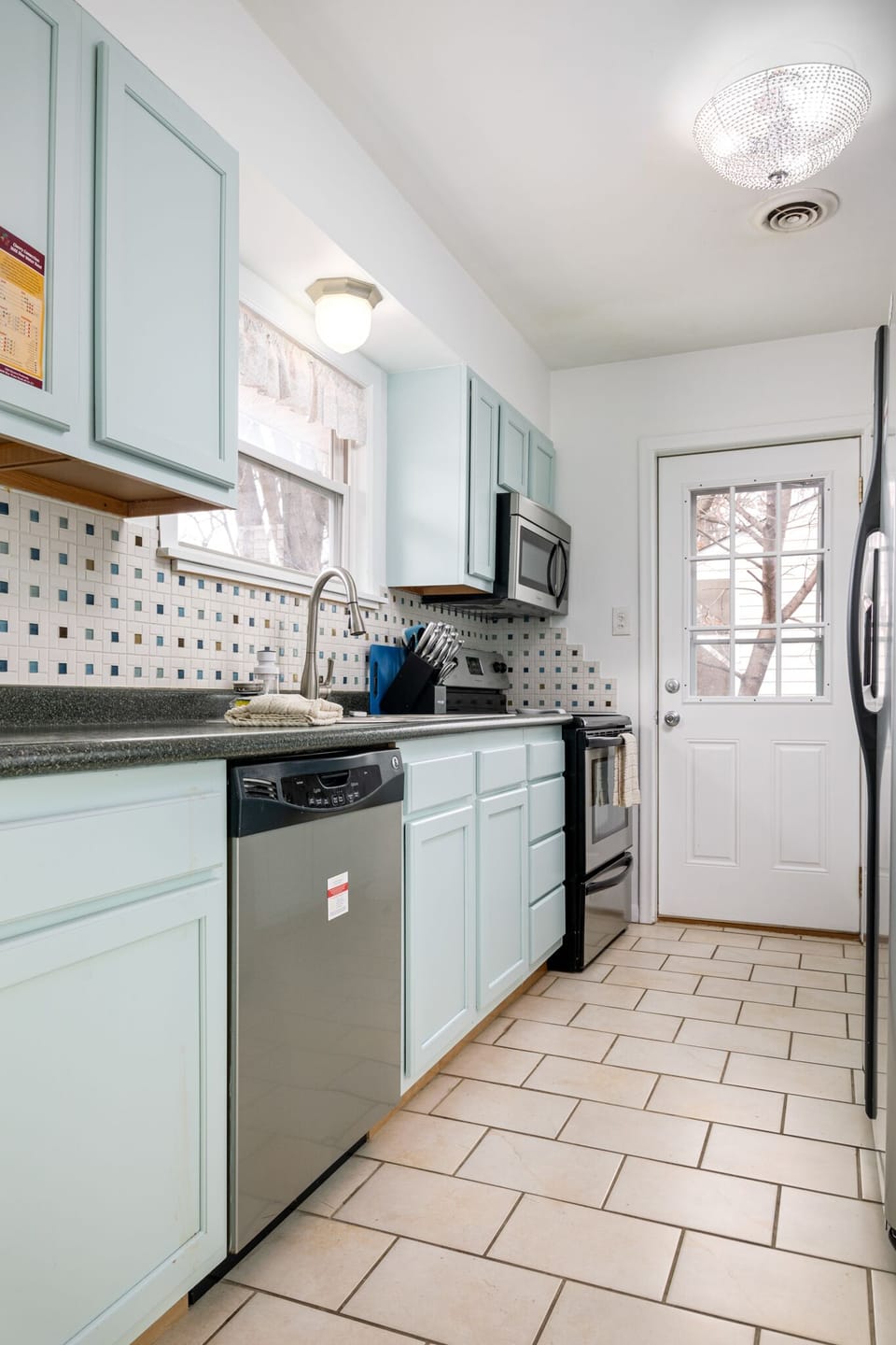 Bright kitchen w/ sleek countertops, modern appliances, & cheerful patterned backsplash