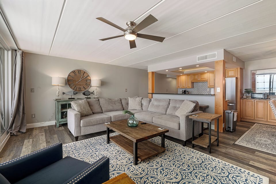 Living room area showing ceiling fan and kitchen in the background