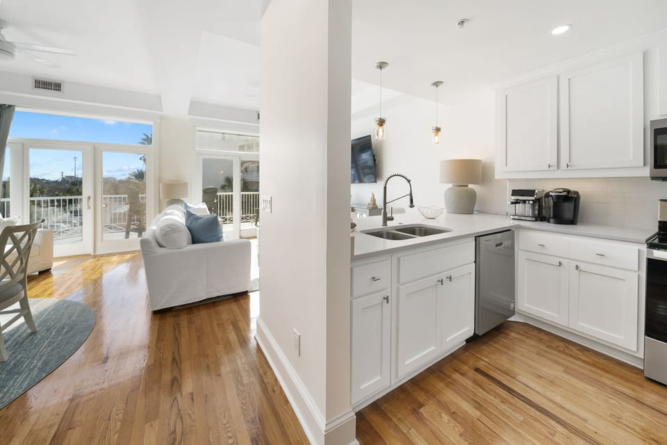 Your bright kitchen flows seamlessly into the living area, where warm hardwood floors and coastal views create the perfect space for cooking and relaxing together.