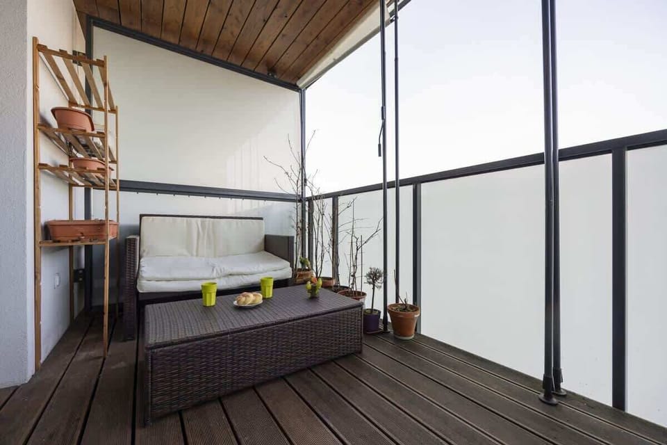 A cozy balcony with a wooden deck, a seating area, and a privacy screen, offering a relaxing outdoor space.

