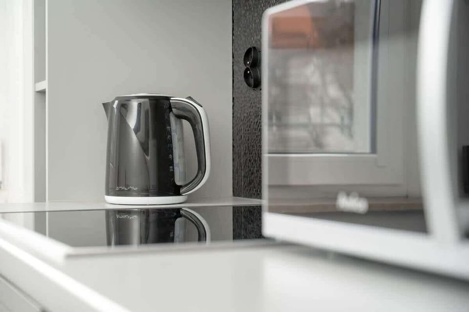 A different angle of the kitchen, showing a large window above the sink, a silver kettle, and a practical workspace.

