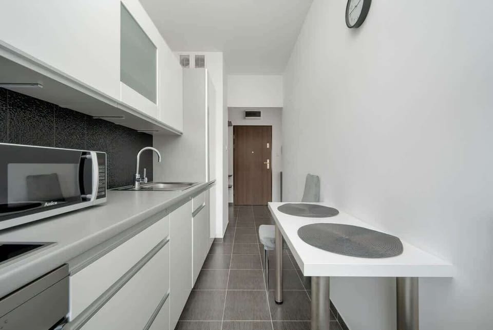 A sleek and minimalist kitchen with white cabinetry, integrated appliances, and a small round dining table for casual meals.

