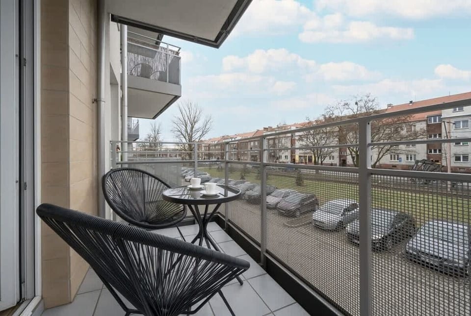 A balcony view overlooking a quiet residential street, featuring black wire chairs for outdoor relaxation.

