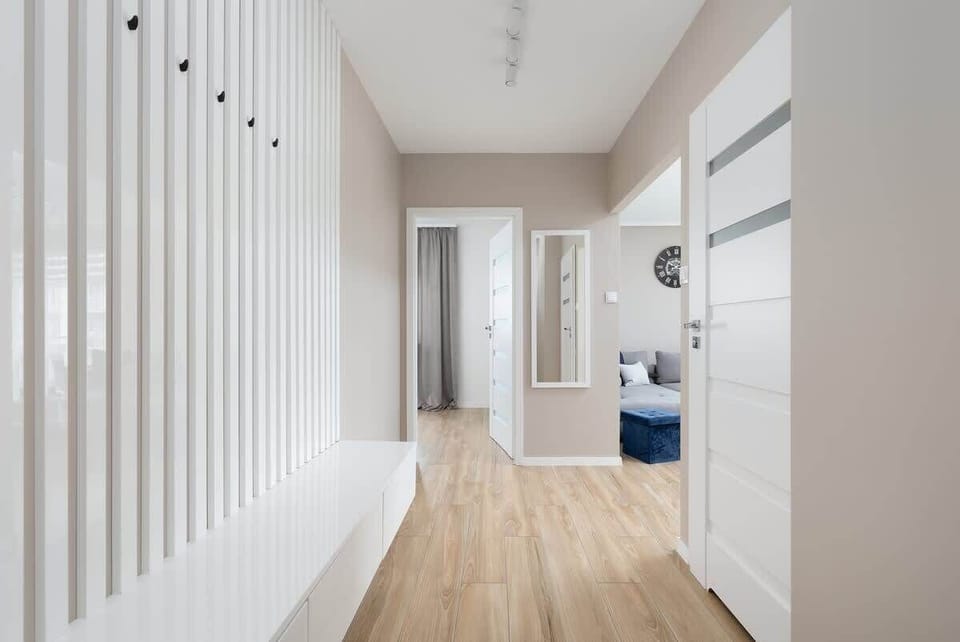 A bright hallway leading to different rooms, with wooden flooring, white walls, and decorative vertical paneling for a contemporary look.

