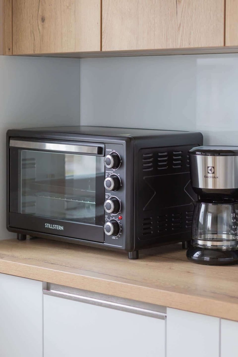 A detailed view of a kitchen countertop, featuring a black toaster oven and a coffee maker, set against a sleek backsplash.


