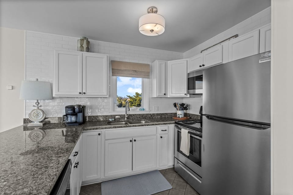 Cook your favorite meals in this bright, fully-equipped kitchen featuring granite countertops, white cabinetry, and modern stainless steel appliances.