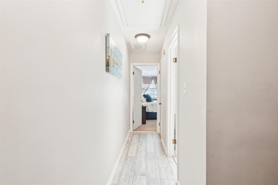 A bright, airy hallway with light wood-style flooring leads to your cozy bedroom, where sunshine and comfort await your arrival.