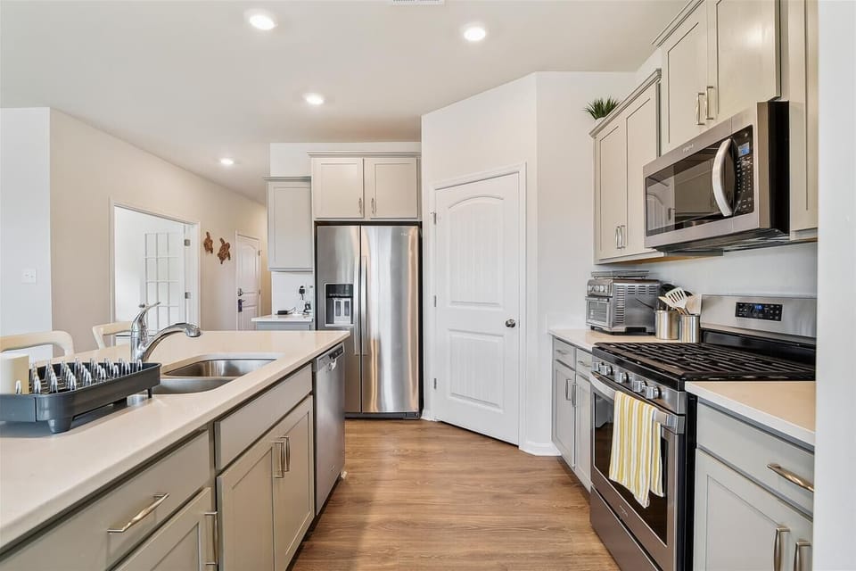 Picture yourself whipping up your favorite meals in this bright, modern kitchen. Stainless steel appliances gleam under warm lighting, sleek countertops offer plenty of prep space, and soft wood floors ground the airy, inviting atmosphere.