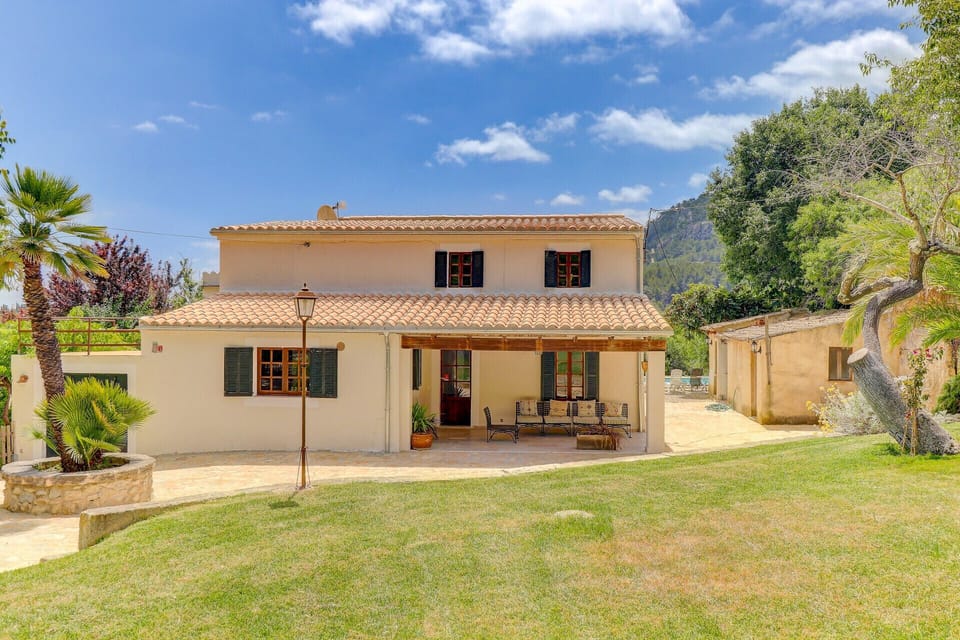 Main façade of  Casa Colonya finca, featuring a covered porch, private garden and rural surroundings with mountain views.