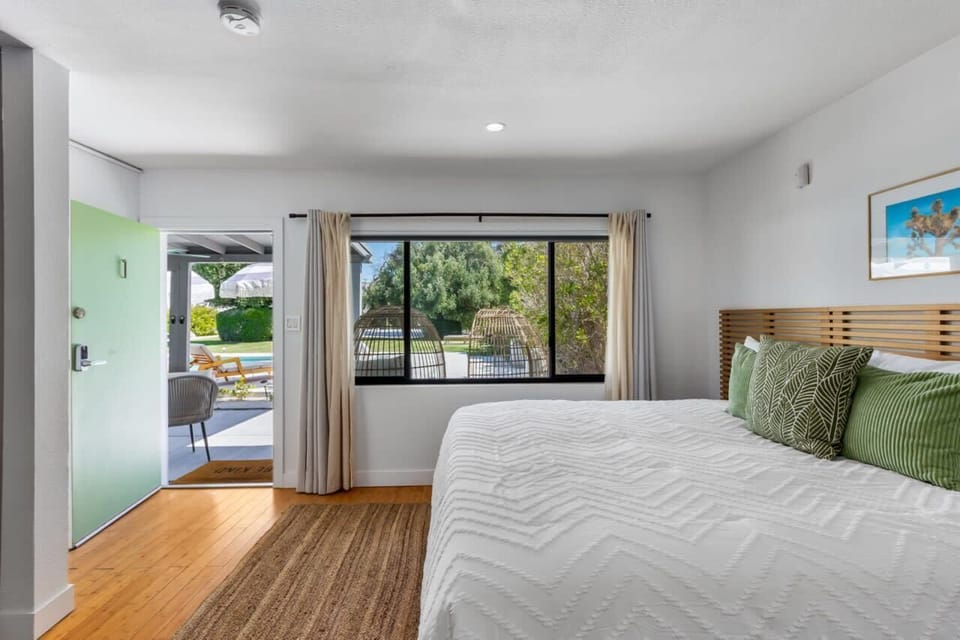 Sunlit bedroom with slatted wood headboard, garden-view window, and direct patio door access to the pool area