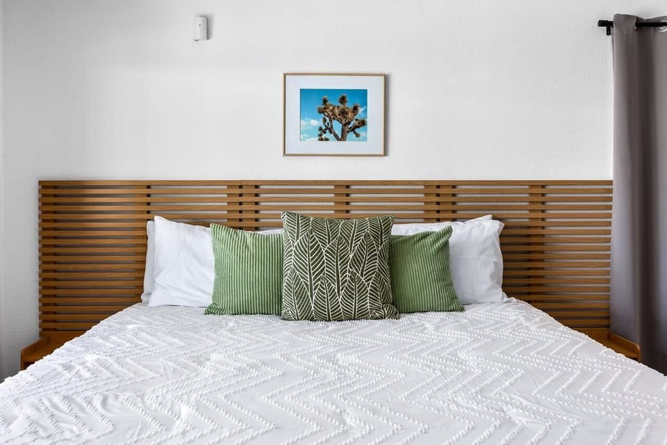 Bedroom with slatted wood headboard, textured white bedding, and desert Joshua Tree art — clean, calm, and very easy to wake up in