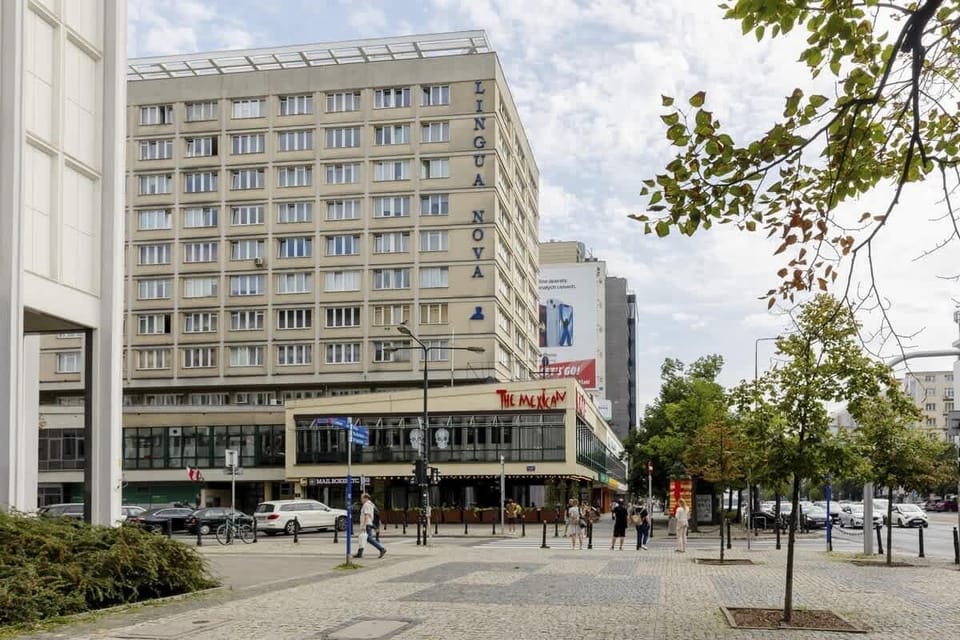 A street view of the surrounding city area, featuring a large commercial building, a pedestrian walkway, and a vibrant urban atmosphere.







