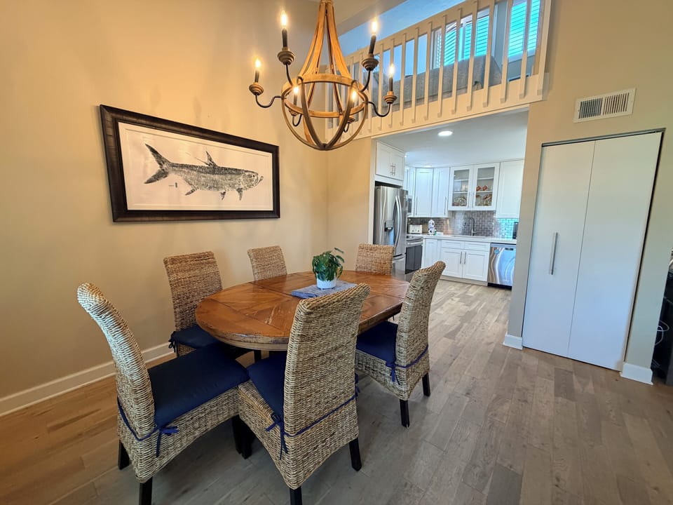 Gather around this inviting dining table where coastal charm meets comfort. A stylish chandelier sets the mood, while the open-concept kitchen beyond promises effortless meal prep and entertaining.