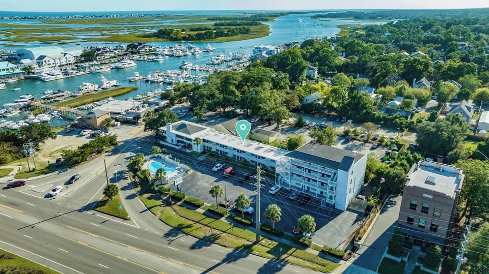 Aerial view of a waterfront property near a marina and coastal wetlands, surrounded by lush greenery and calm waterways.