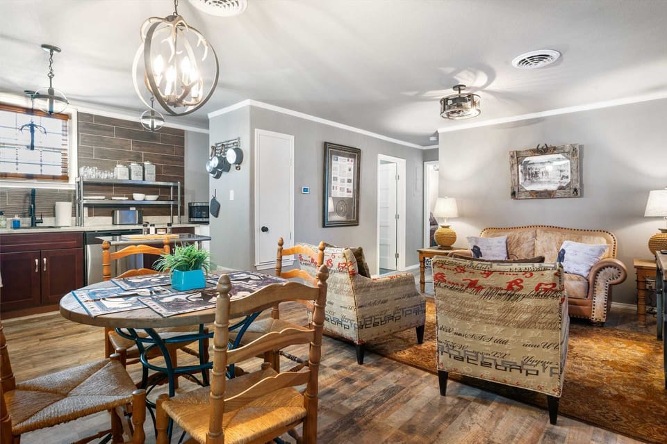 An eclectic, rustic living and dining area featuring antler-style lighting, wood-paneled accents, and a mix of vintage-patterned seating for a cozy, western-inspired atmosphere.