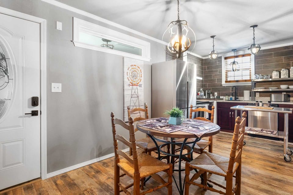 A rustic dining nook featuring a round wood table with woven-seat chairs, an antler chandelier, and a backdrop of a modern kitchen with dark wood-look tiling.