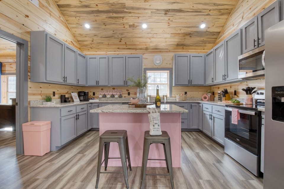 Fully equipped kitchen with a pink island, coffee bar, and warm cabin-style woodwork.