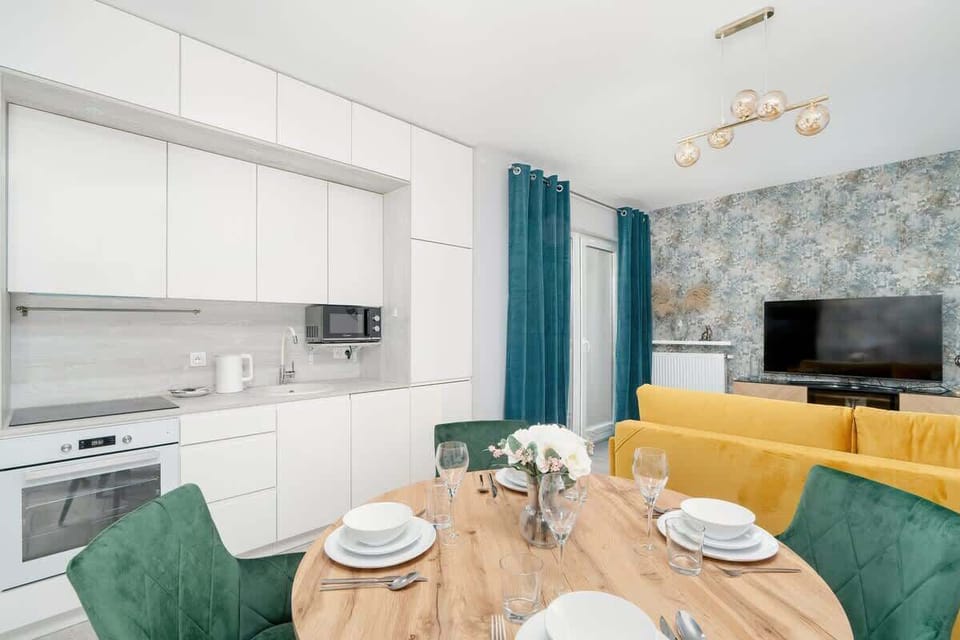 A sleek open-plan kitchen and dining area with white cabinets, a wooden table, and dark green chairs, creating a sophisticated look.


