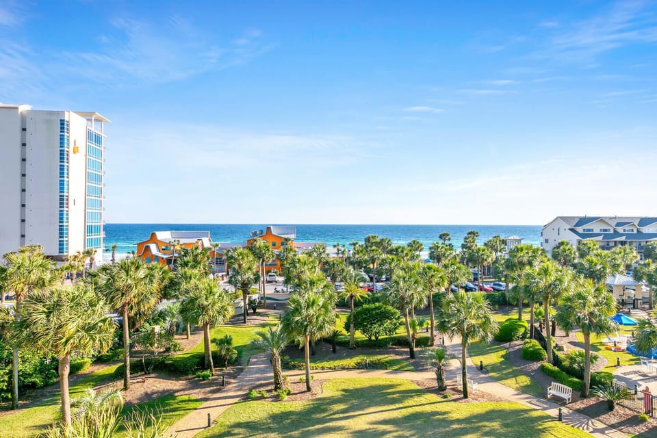 Elevated view showcasing the coastal location with palm trees, nearby buildings, and ocean access in the surrounding area.