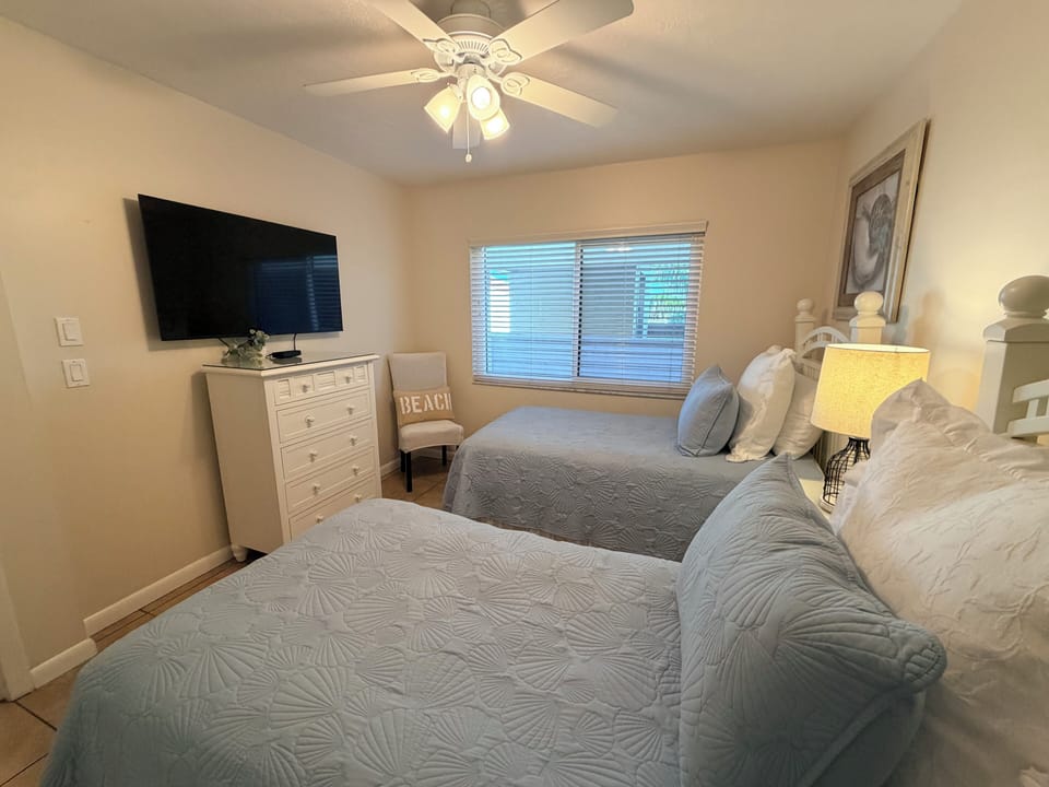 Rest comfortably in your bright bedroom with two queen beds, featuring a ceiling fan, flat-screen TV, and coastal decor for a peaceful night's sleep.