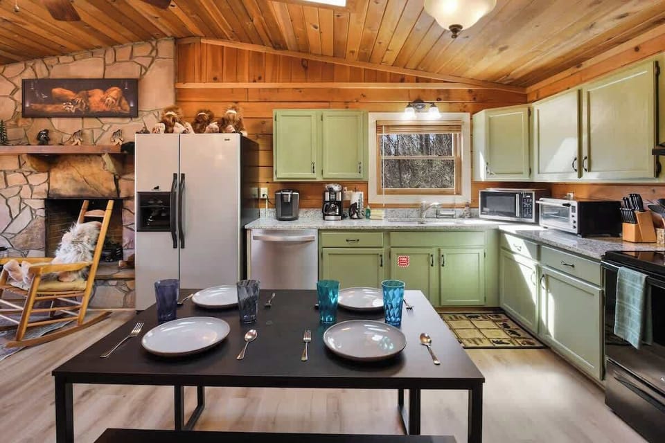 Rustic kitchen with green cabinetry, modern appliances, and a cozy stone fireplace.