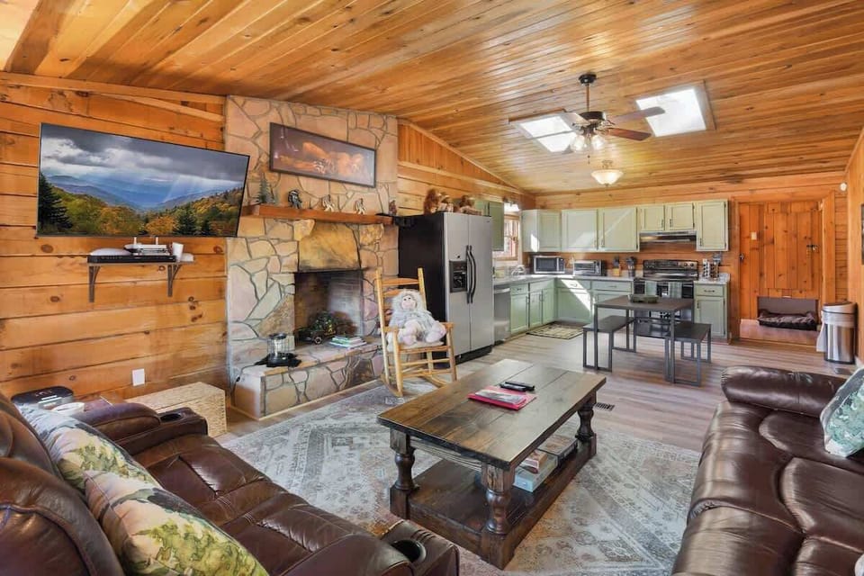 Cozy rustic living area with stone fireplace and open kitchen featuring green cabinetry.