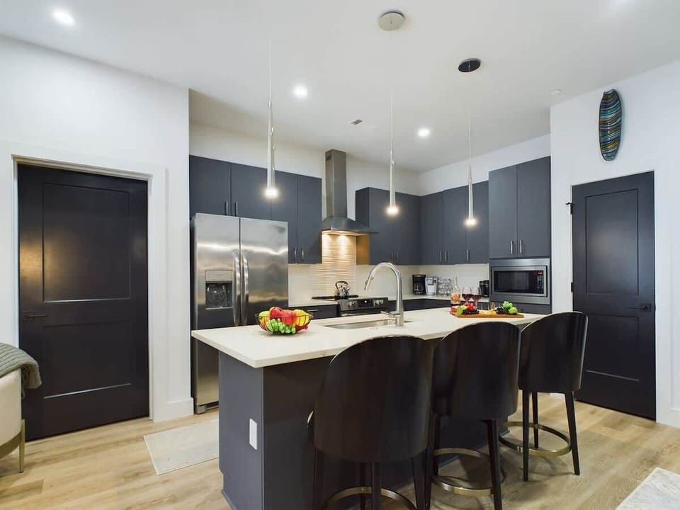 Fully equipped kitchen with stainless steel appliances, basic cooking essentials, toaster, coffee machine, kitchen island seating, and breakfast table for 2.
